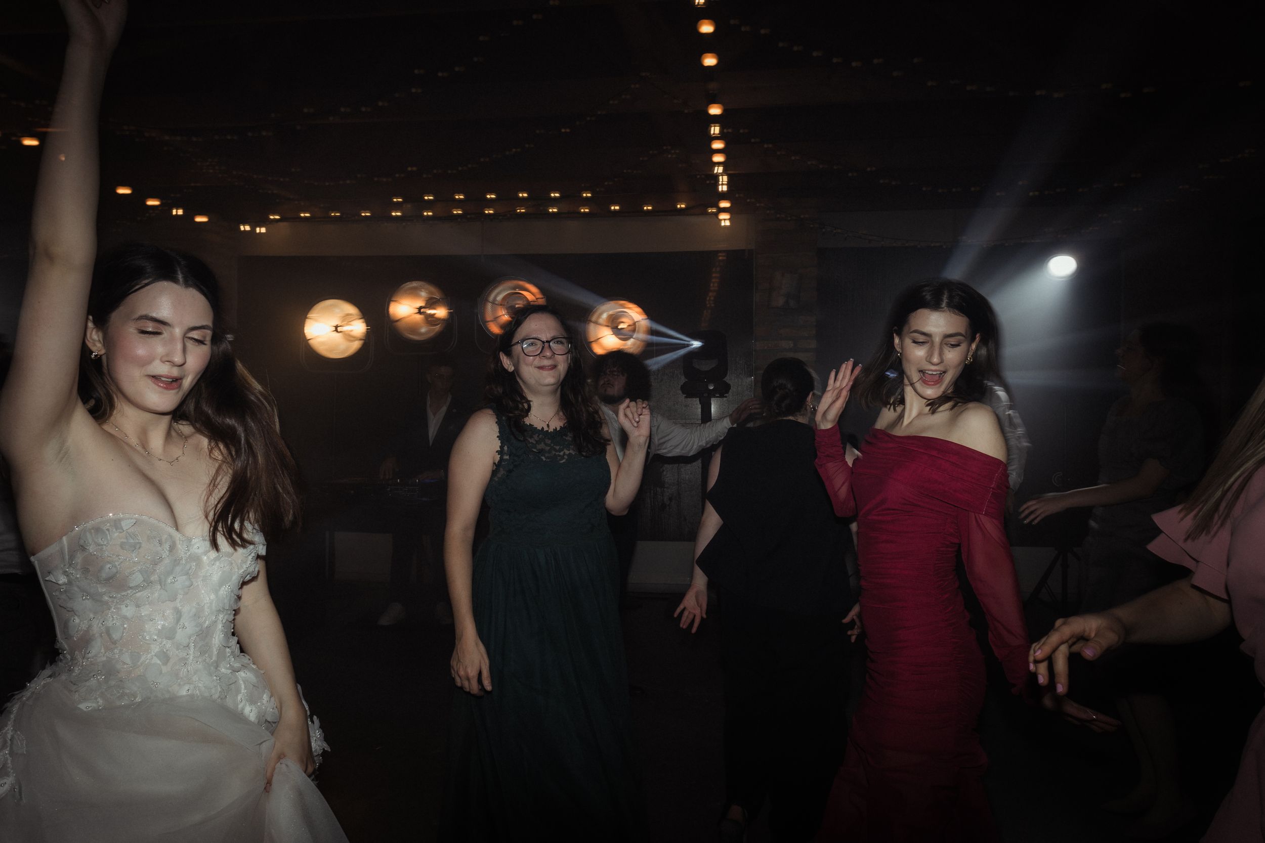 People dancing and socializing at a dimly lit party or reception venue with string lights overhead.