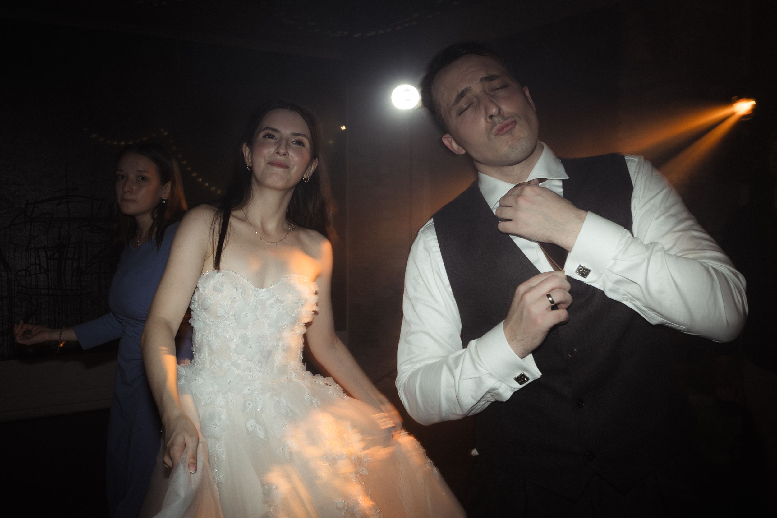 A couple dances together in formal attire under dim lighting at a wedding reception.