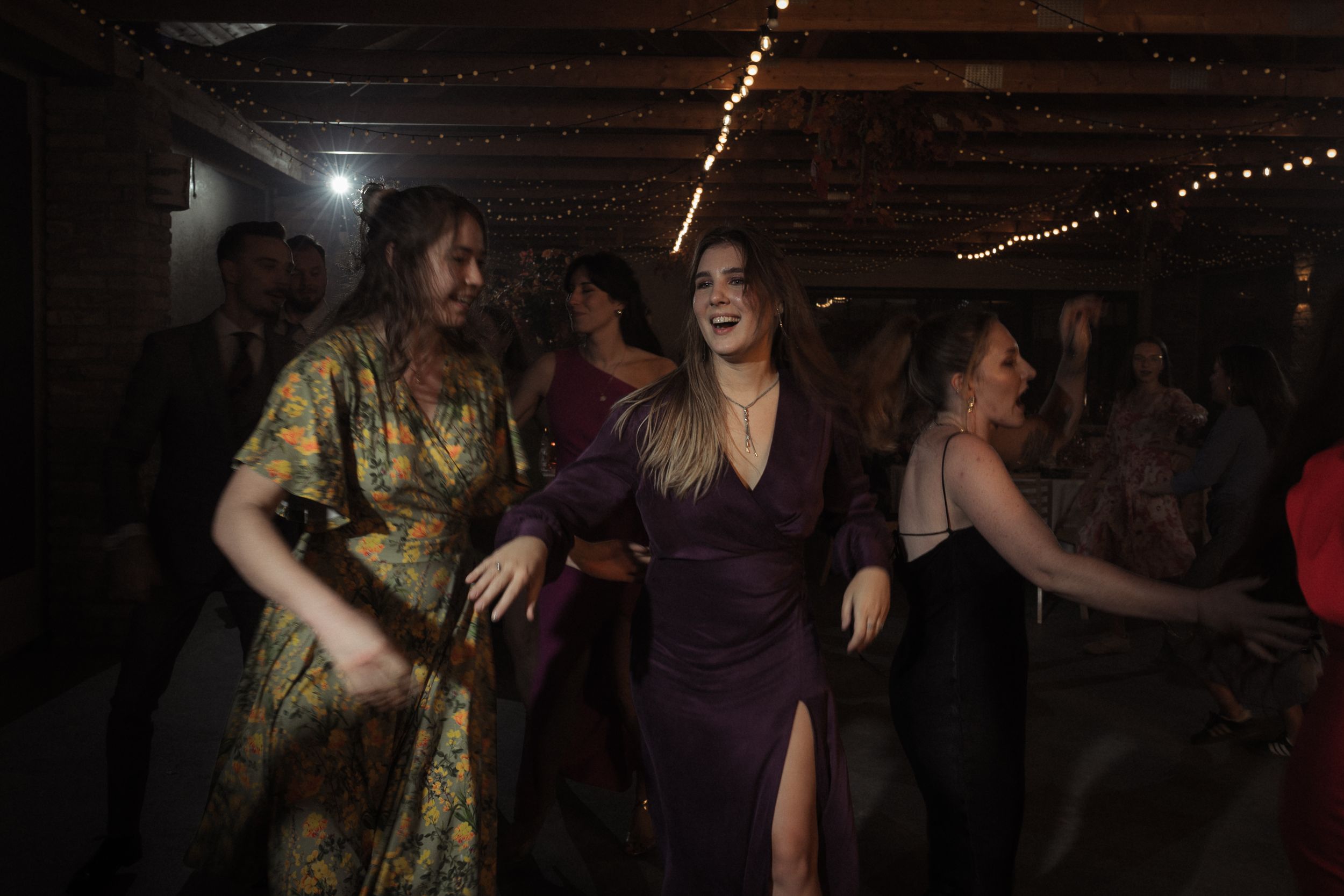 People dancing together at a dimly lit party venue with string lights in the background.