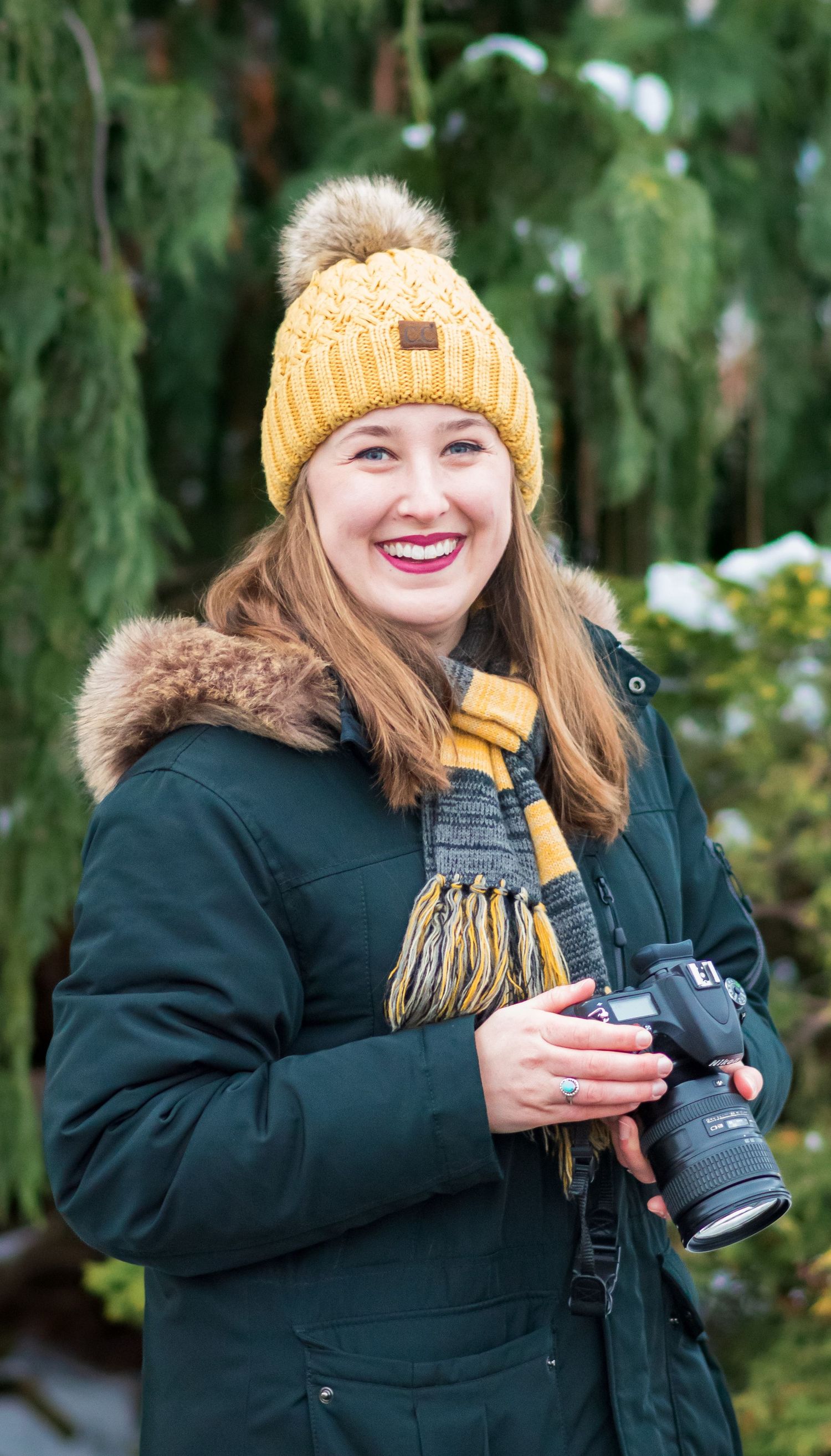 Photographer wearing yellow beanie and winter coat holding camera outdoors.