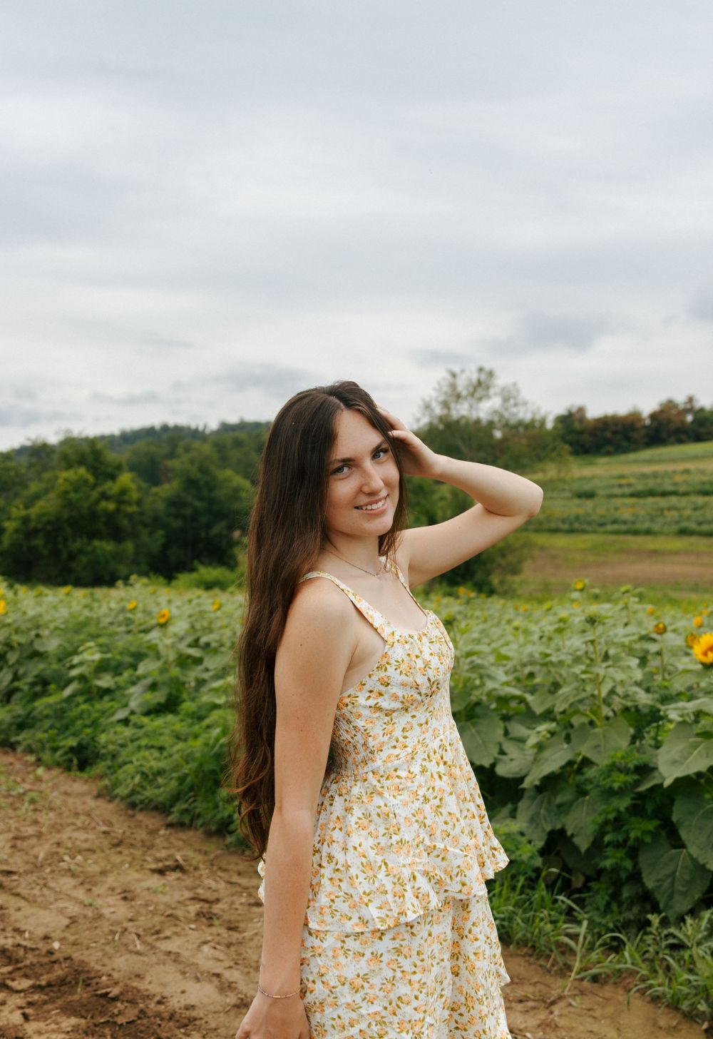 Person in floral dress poses joyfully in a sunny farm field.