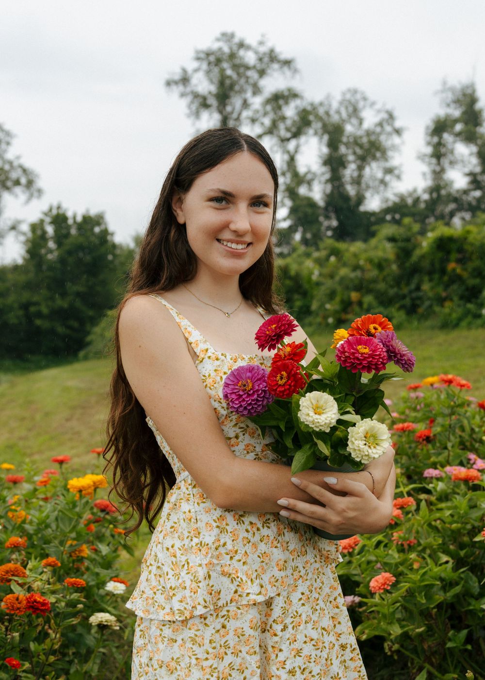 A summer garden photoshoot features someone holding freshly picked flowers while wearing a floral dress.