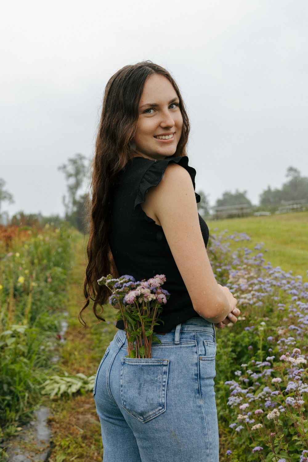 Person in casual outfit smiles while holding wildflowers in a blooming meadow.