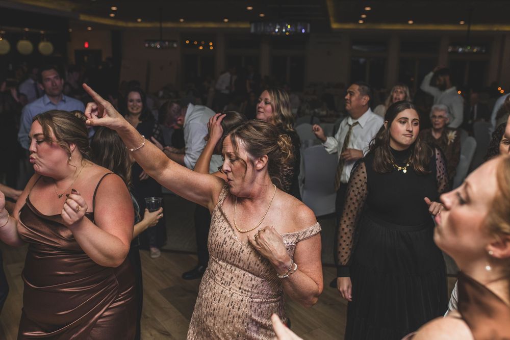 A group of wedding guests dance and celebrate together on a dimly lit dance floor during a reception.
