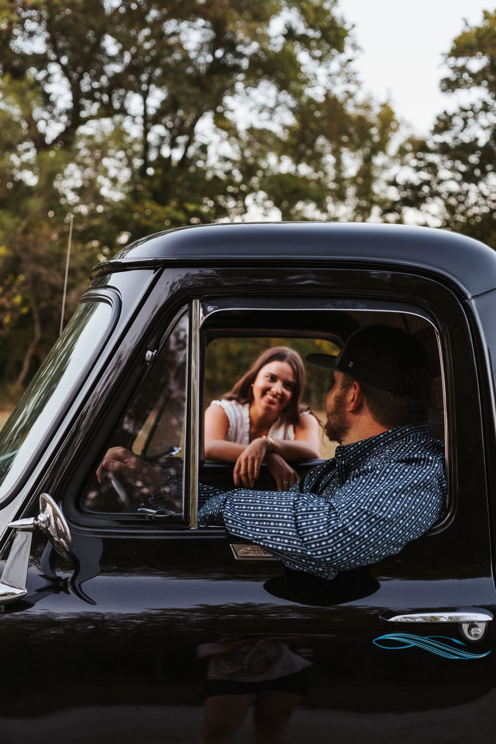 A couple shares a joyful moment together in a vintage black pickup truck on a sunny day.
