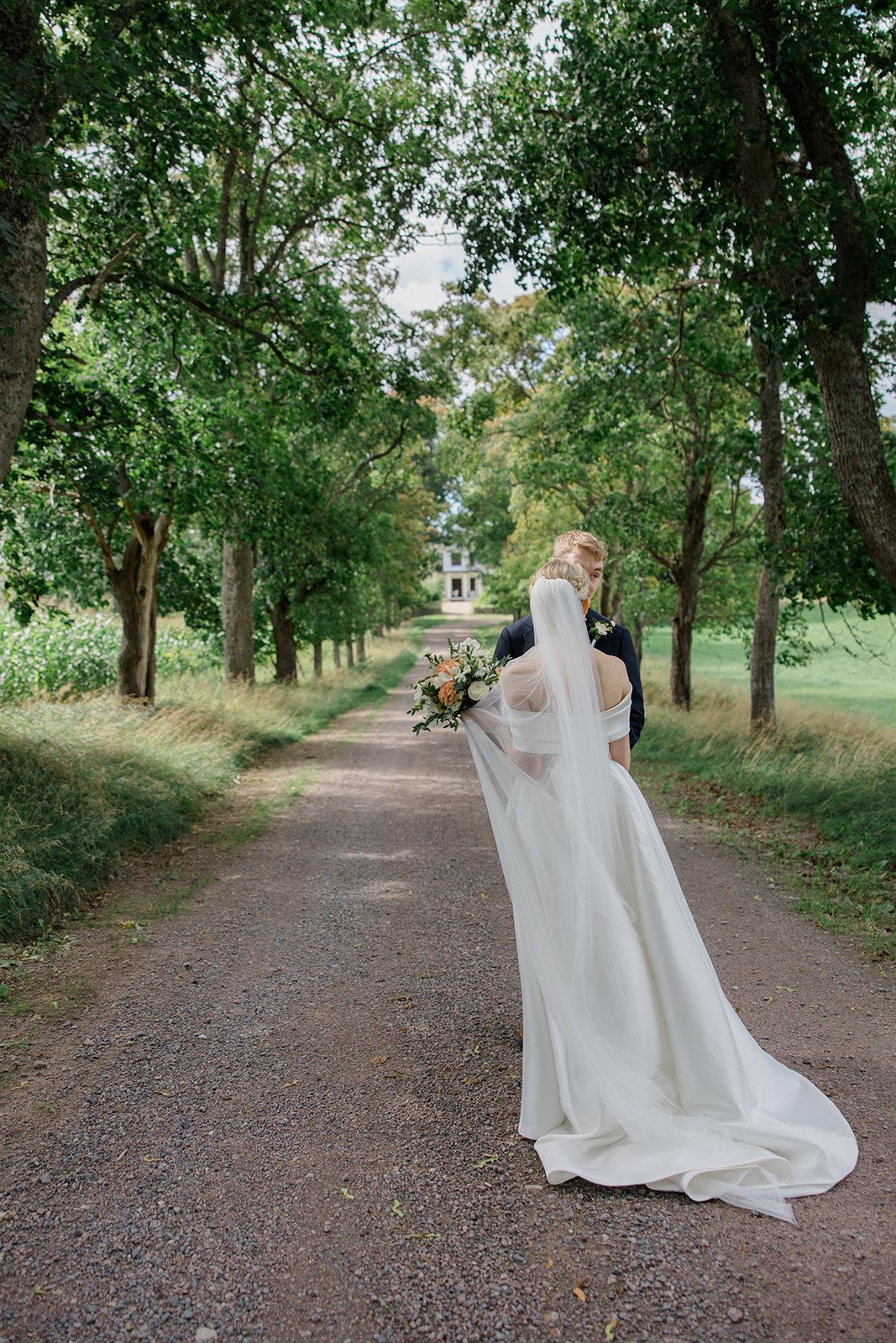 A flowing white wedding veil billows dramatically in black and white as it trails behind the bride outdoors.