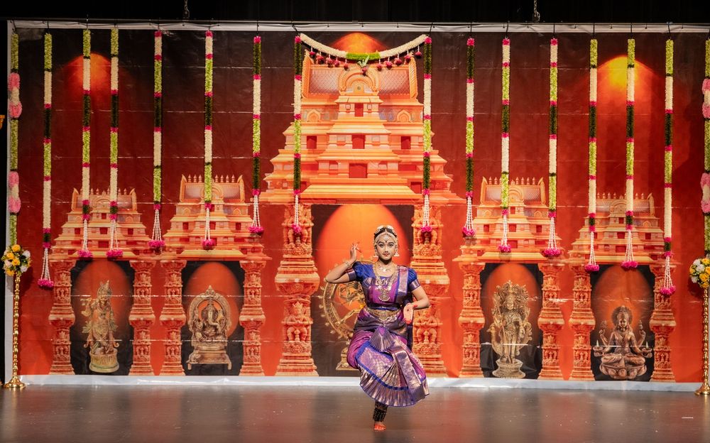 Dancers perform on stage against a backdrop of ornate red and gold temple-like structures with illuminated lighting.
