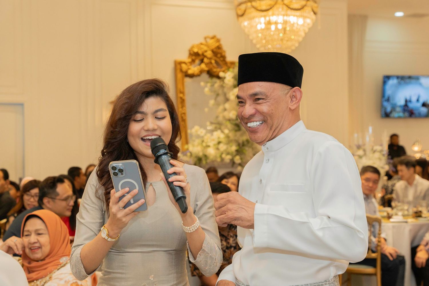 Wedding guests taking photos and socializing at an elegant reception venue with golden lighting.