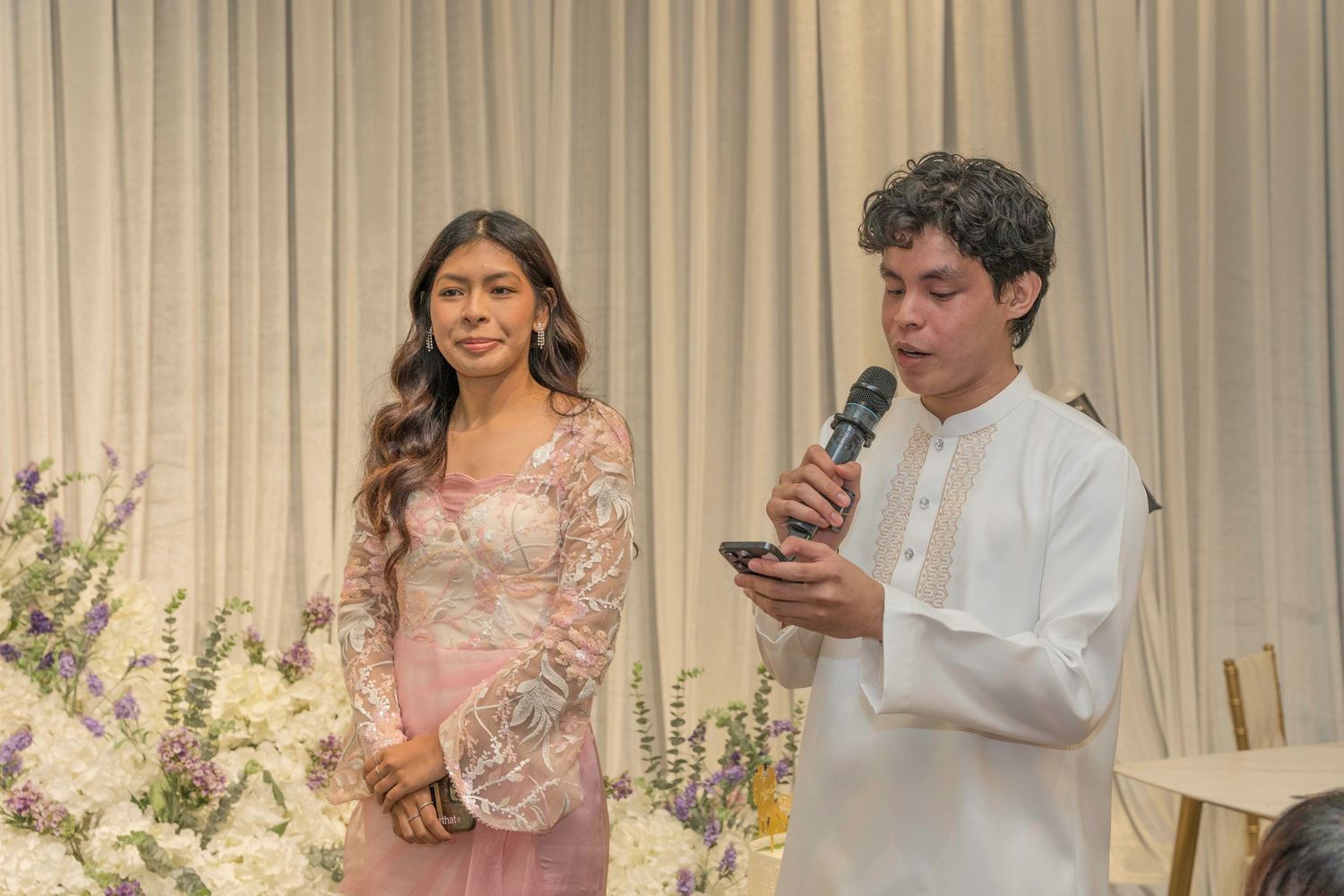 Wedding guests mingling and taking photos at a reception with floral decorations.