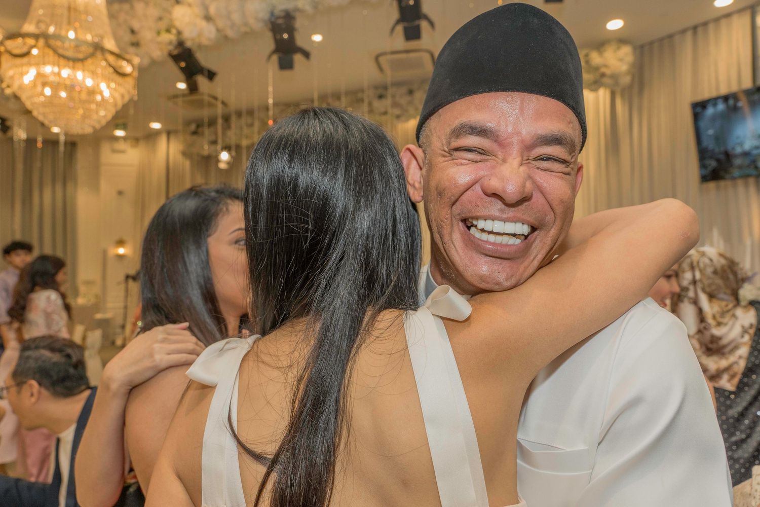 Joyful celebration with guests smiling and embracing at wedding reception.