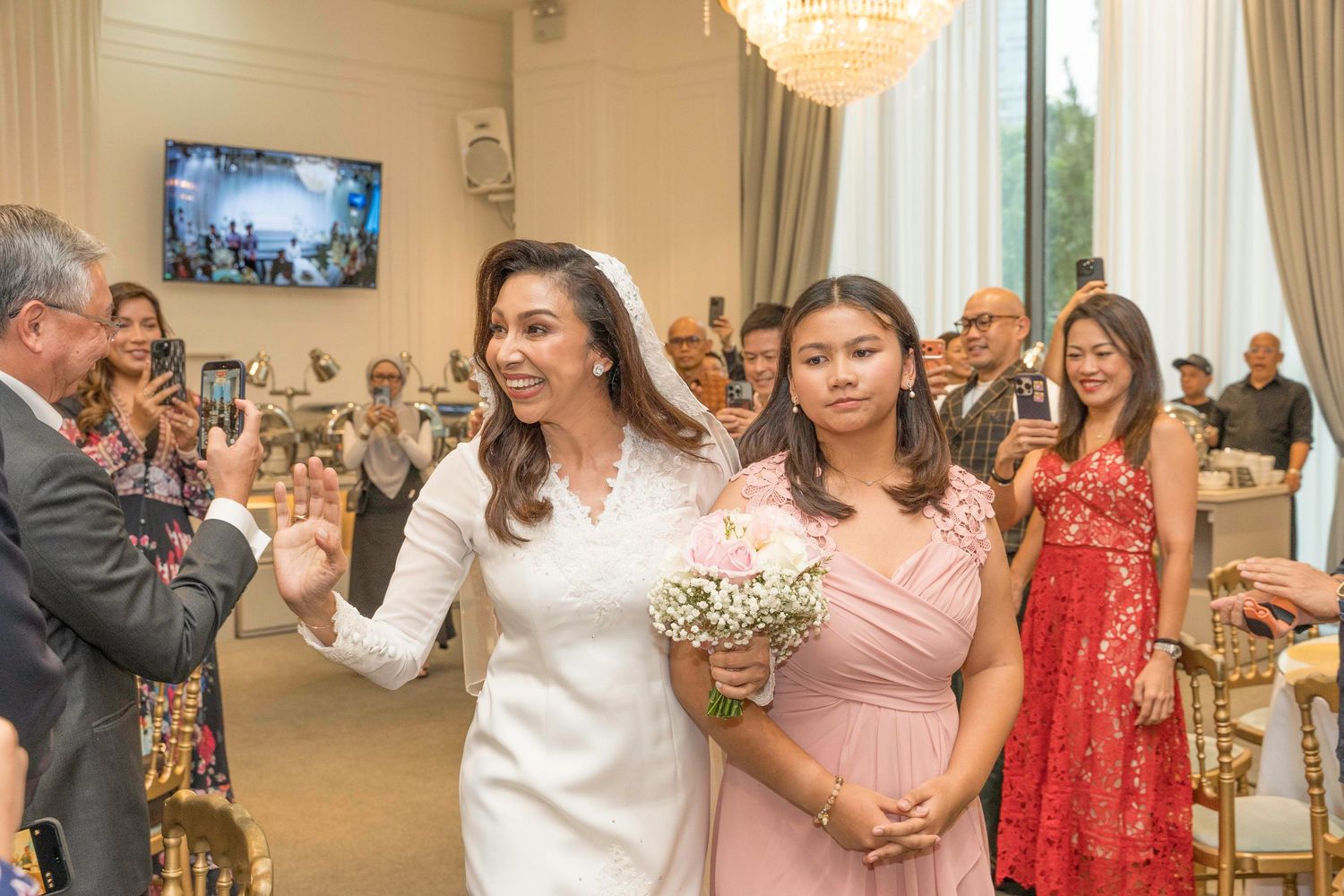 Wedding celebration in an elegant ballroom with chandelier and white drapes.