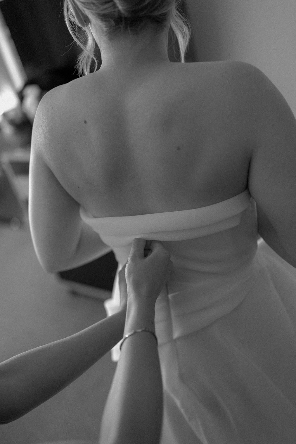 Black and white artistic photo showing the back of someone wearing a strapless white dress.