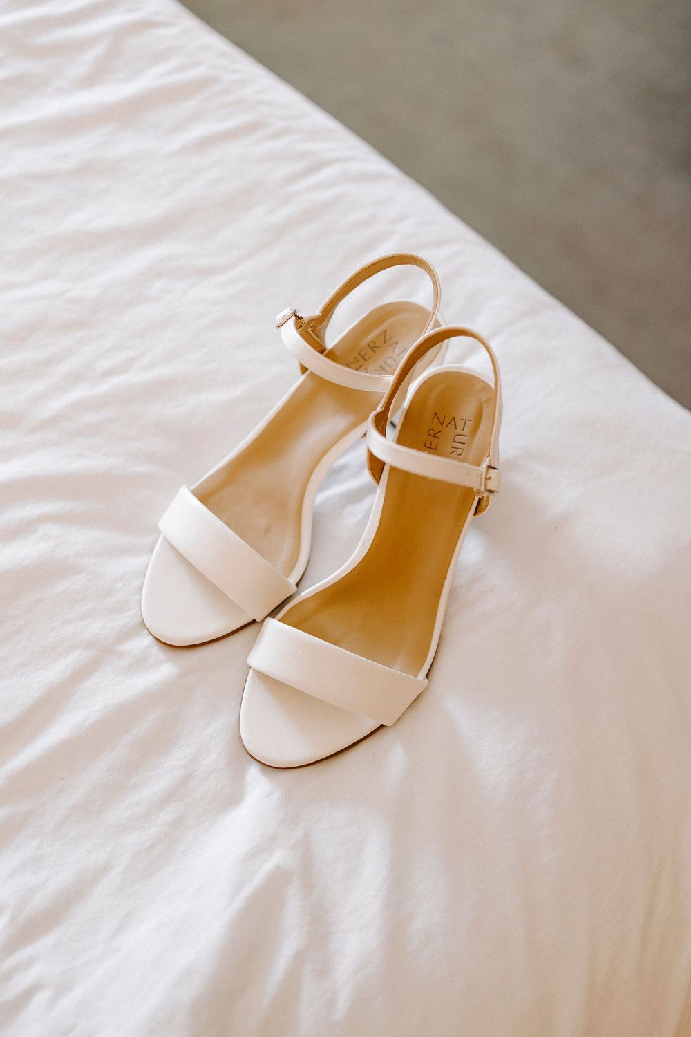White leather slingback sandals with ankle straps displayed on a white fabric surface.