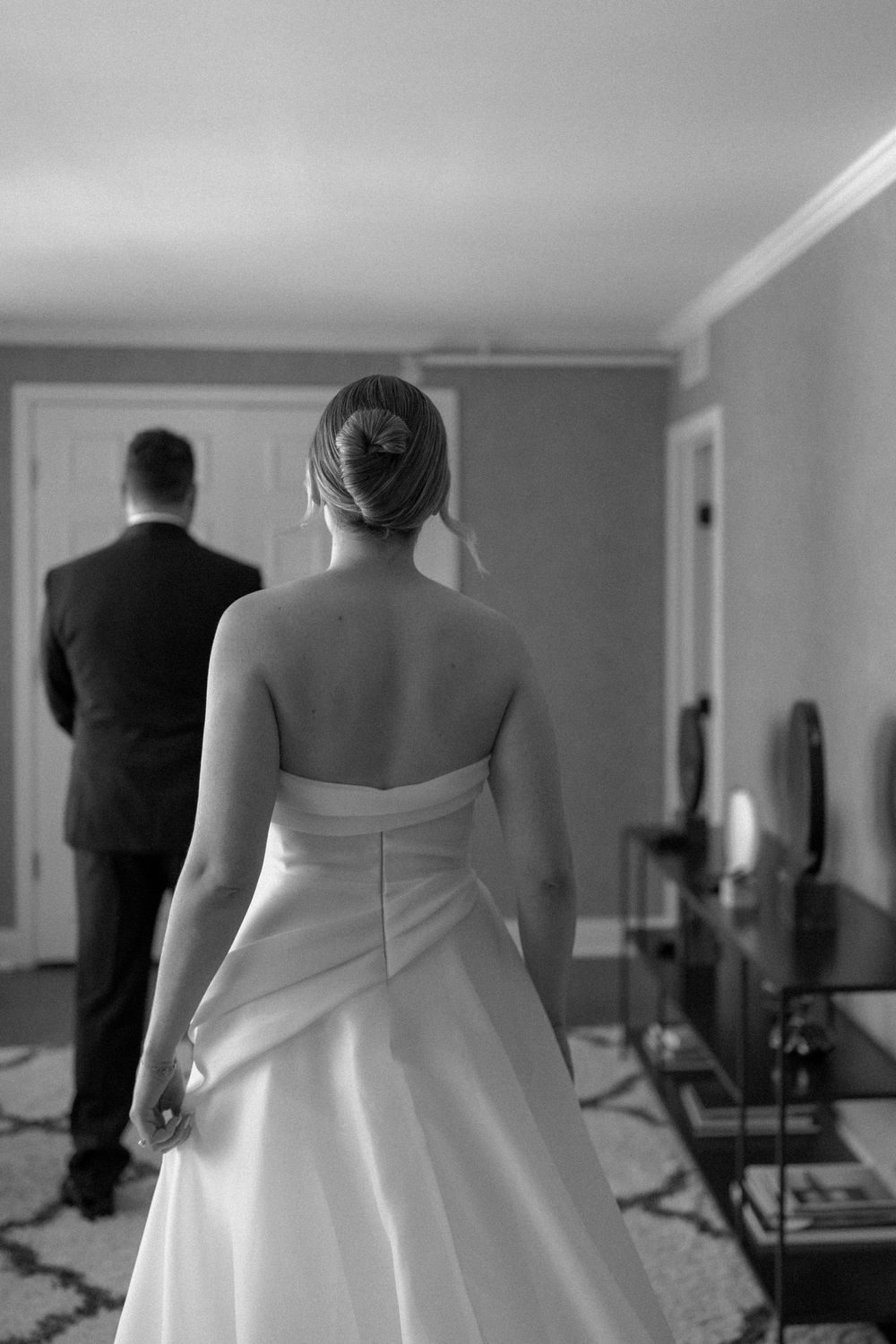 Black and white photograph showing a sequence of wedding dress details from behind in a hotel room.