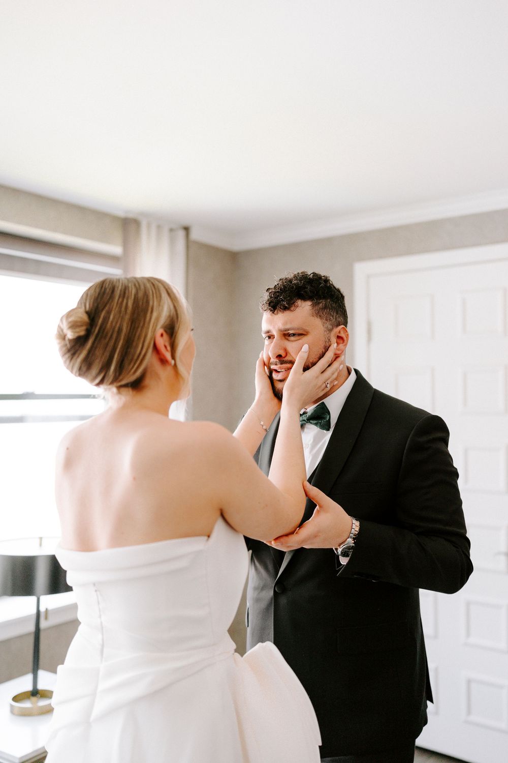 Emotional first look moment between a couple in formal wedding attire in a bright room.