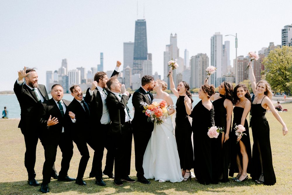 Wedding party celebrates with raised arms against Chicago skyline backdrop on a sunny day.