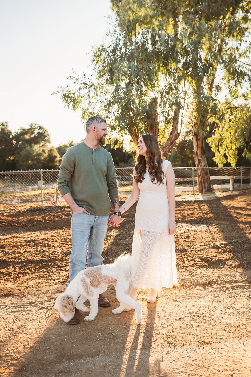 A couple and their fluffy white dog enjoy a sunset photoshoot in a rustic outdoor setting.