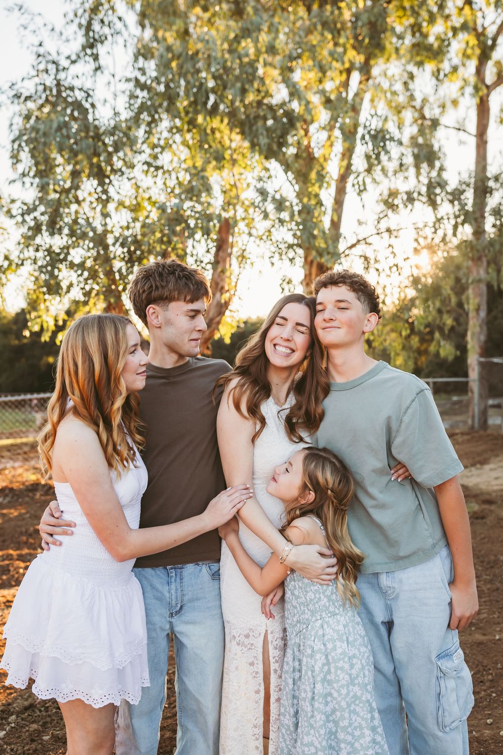 A joyful group in coordinated blue and white outfits poses together in a natural outdoor setting during golden hour.