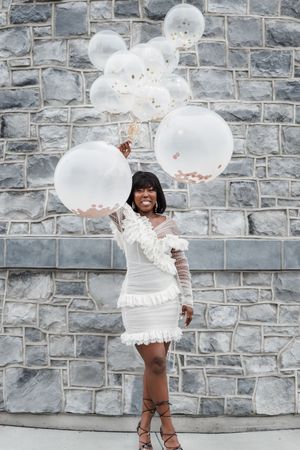 A joyful celebration with white balloons against a grey stone wall backdrop.