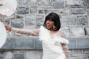 Person in white lace dress poses against stone wall background.