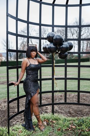 Glamorous photo shoot featuring sparkly black gown and balloons against an outdoor metal gazebo structure.