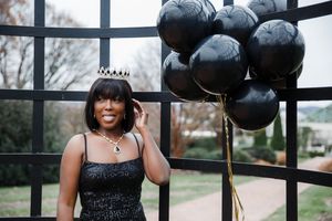 A series of black balloons float against a window backdrop creating a moody and dramatic photoshoot setting.