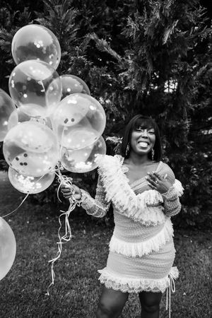 Black and white portrait with white balloons and frilly dress creating joyful celebration mood.
