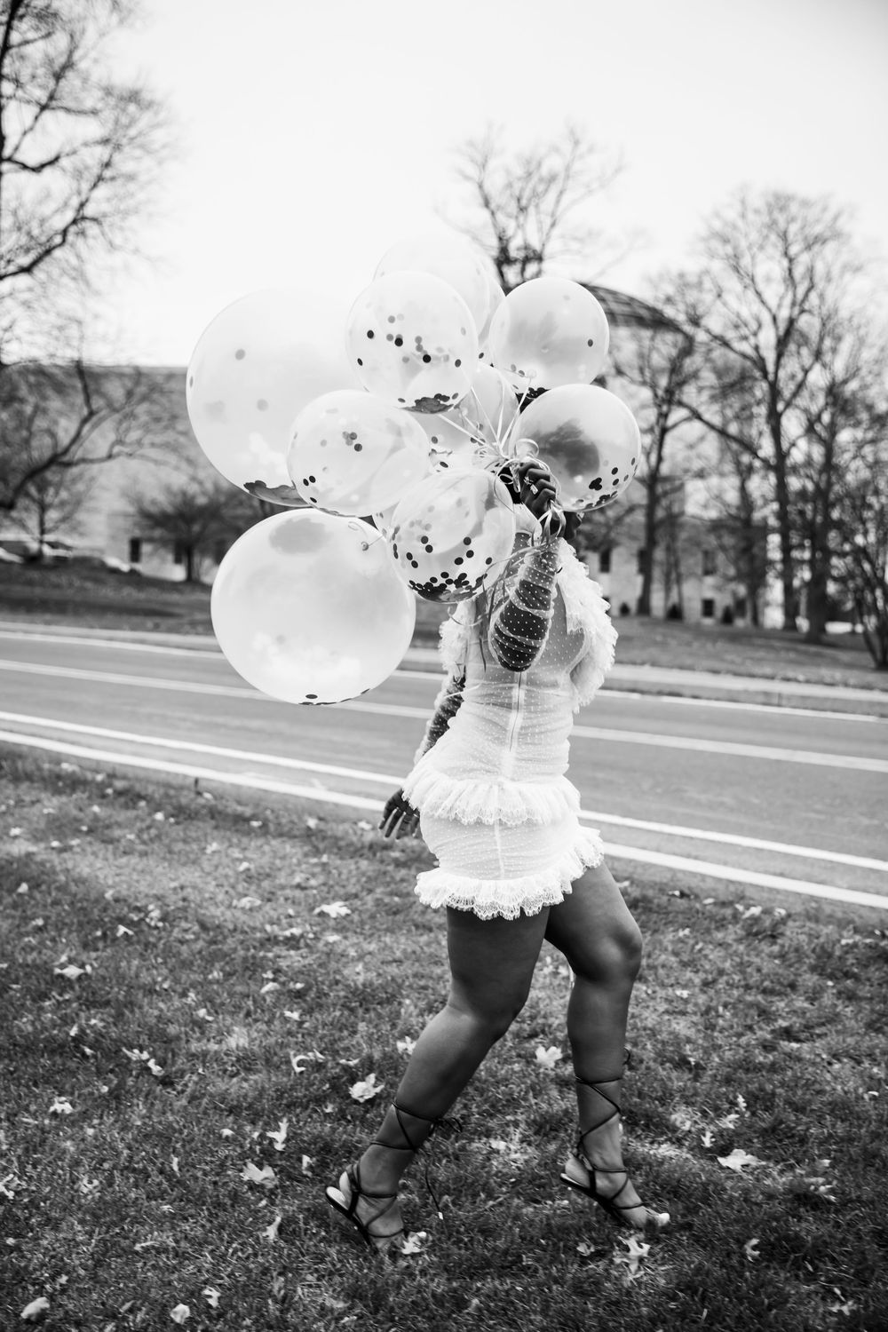 Black and white photo of someone holding white balloons while dancing outdoors.