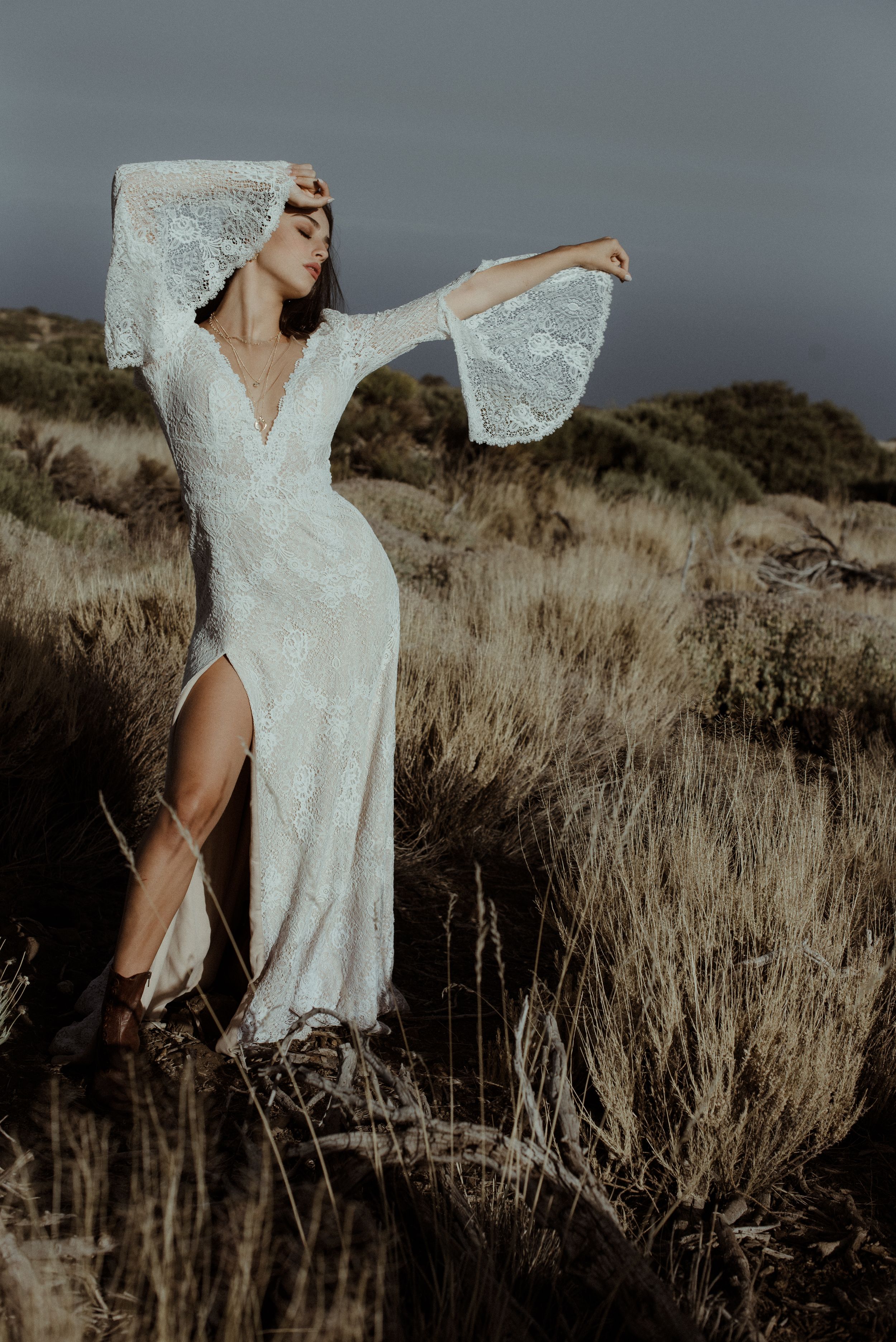 Flowing white lace wedding dress with dramatic bell sleeves and thigh slit captured in desert setting.
