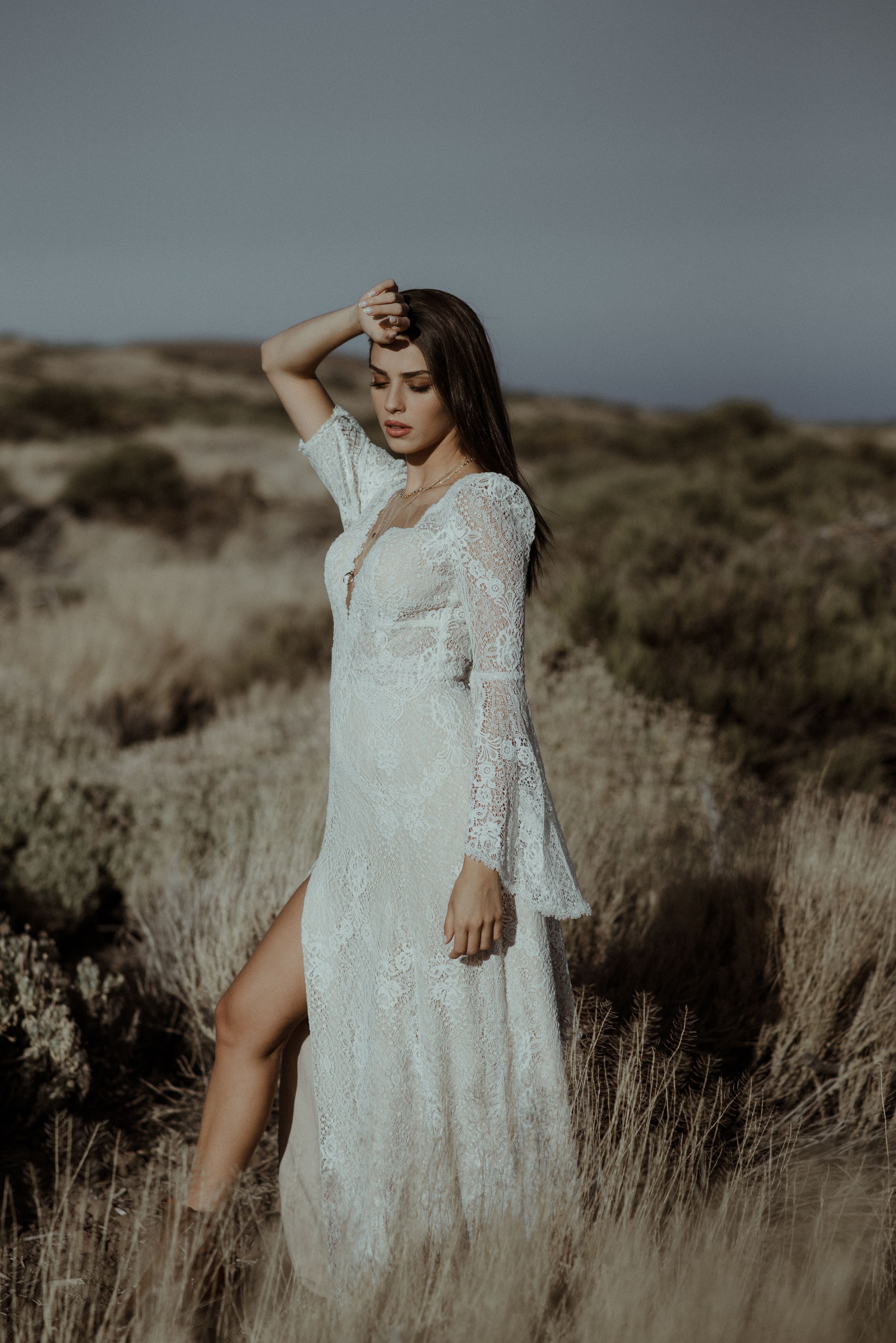 A white lace wedding dress with long sleeves photographed in a desert landscape at dusk.
