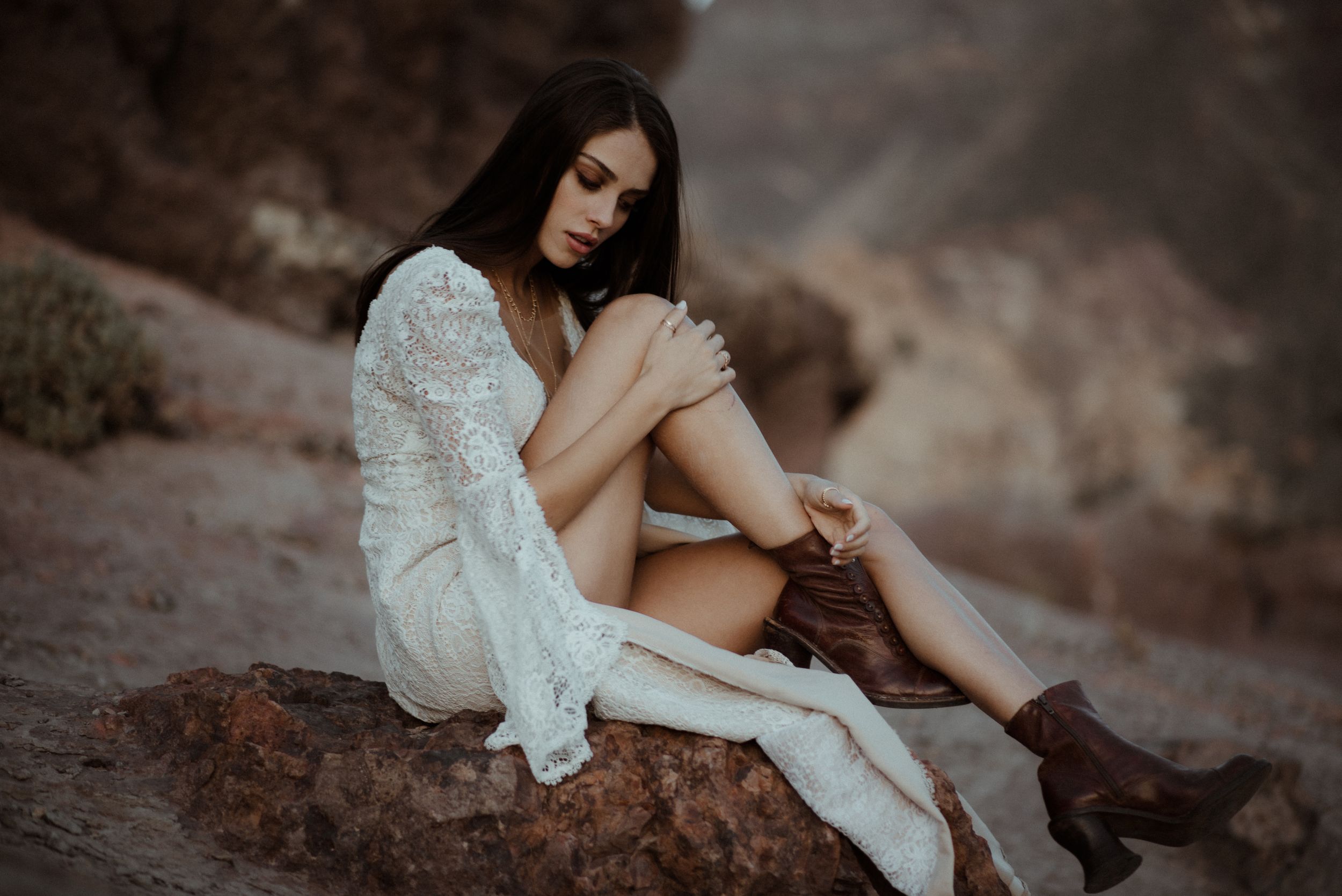 Ethereal bridal portrait showing delicate white lace dress and boots against rocky desert terrain.