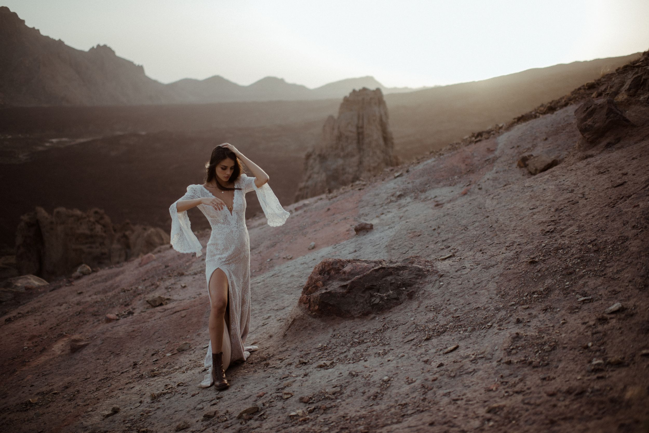 Romantic bridal portrait in white lace dress amid desert mountains at sunset.