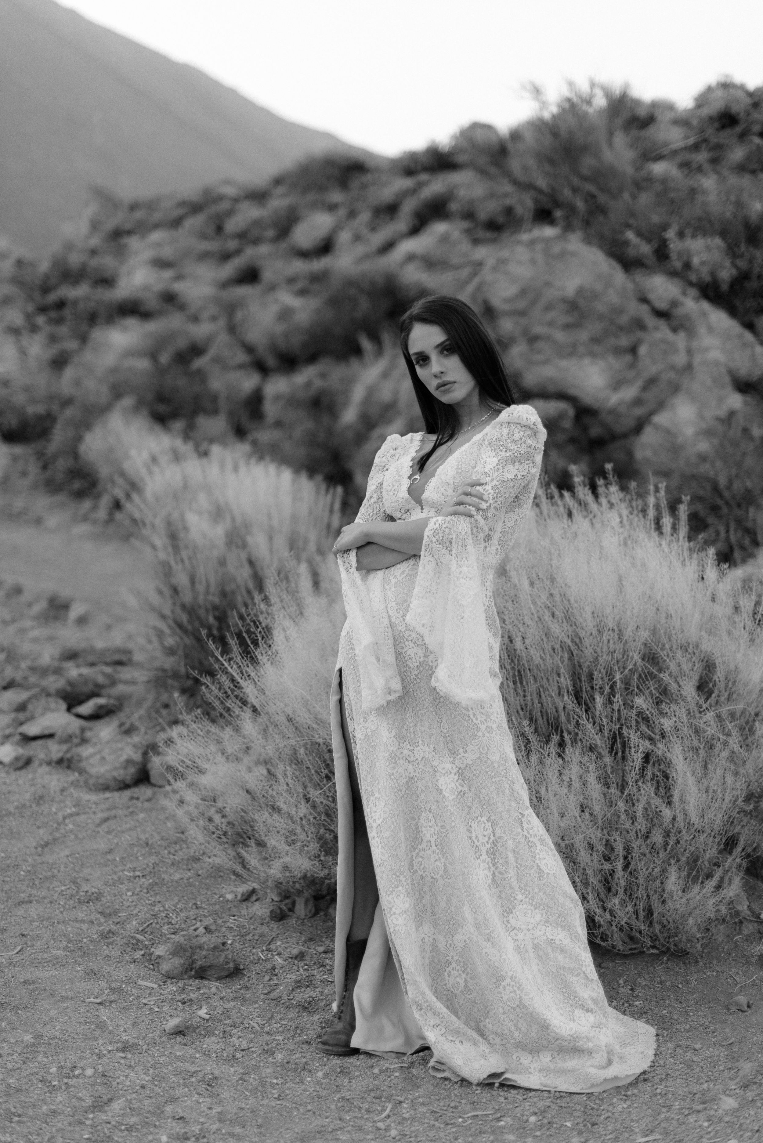Classic black and white bridal portrait featuring lace wedding gown against desert brush landscape.
