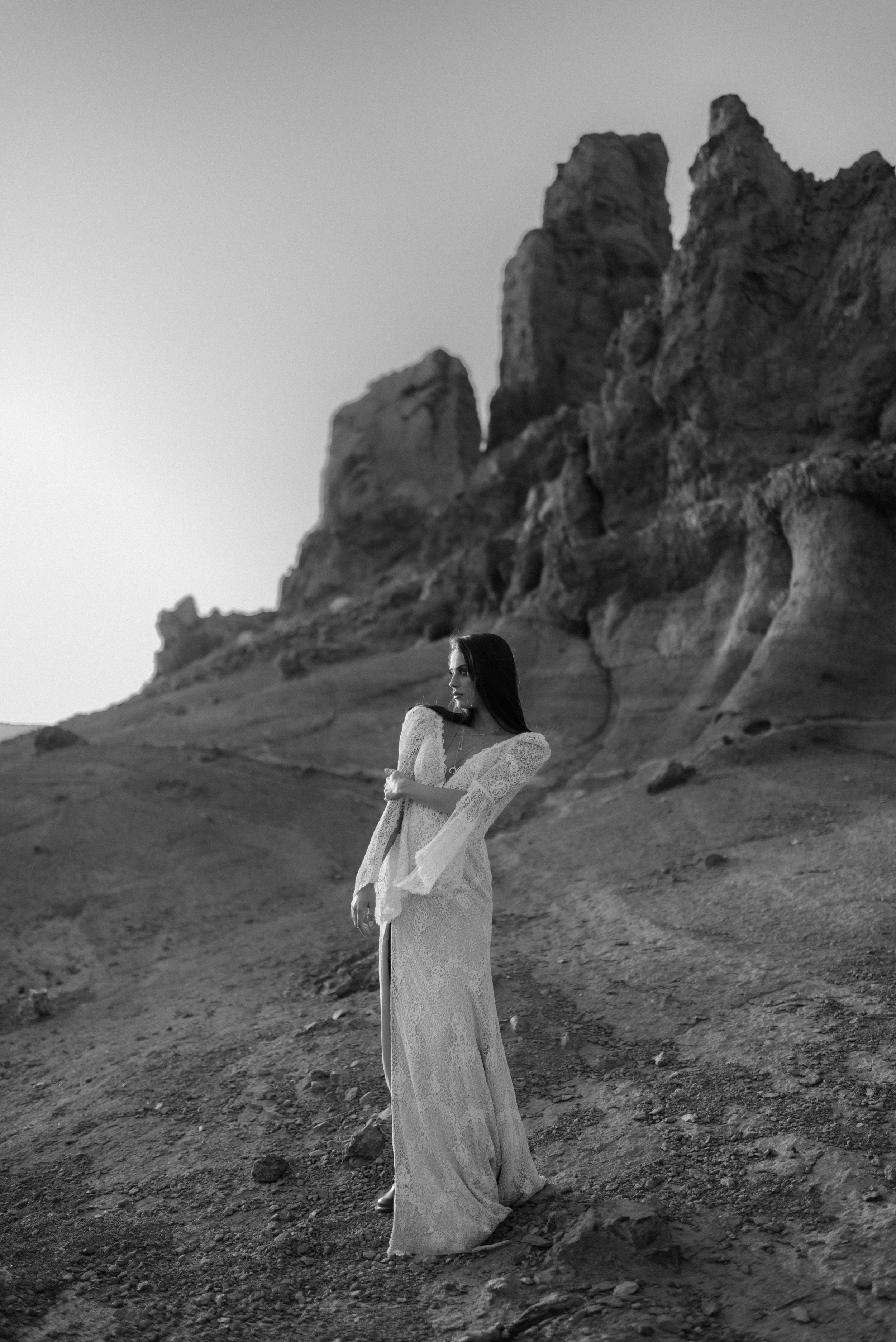 A person in a flowing white dress poses dramatically against towering rock formations in black and white.