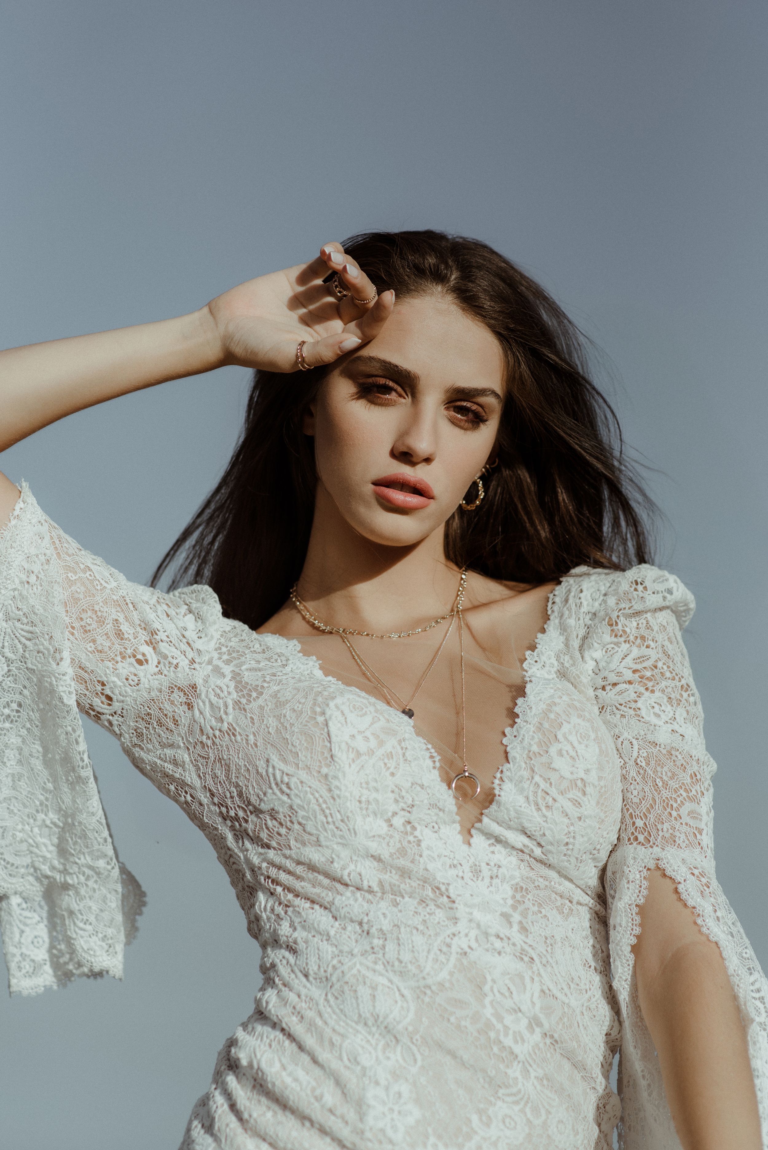 Elegant white lace wedding gown with dramatic V-neckline and flared sleeves photographed against grey backdrop.