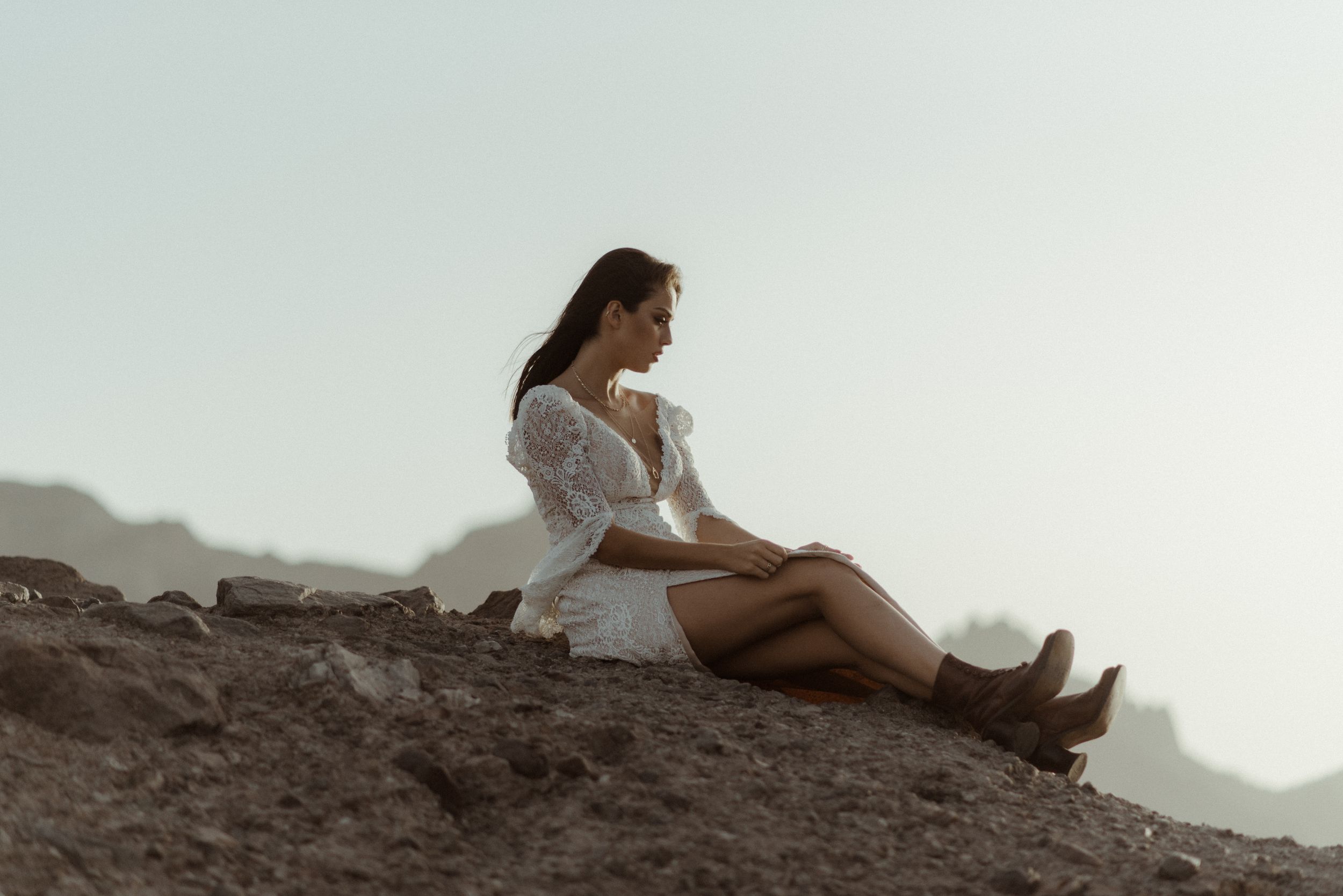 Person in white dress sitting on mountainside during golden hour.