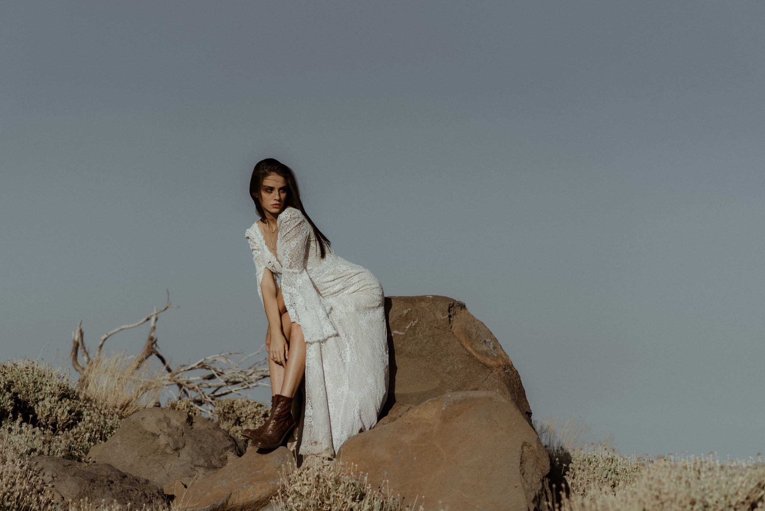 A dreamy desert photoshoot featuring someone in a white dress perched on a rocky outcrop.