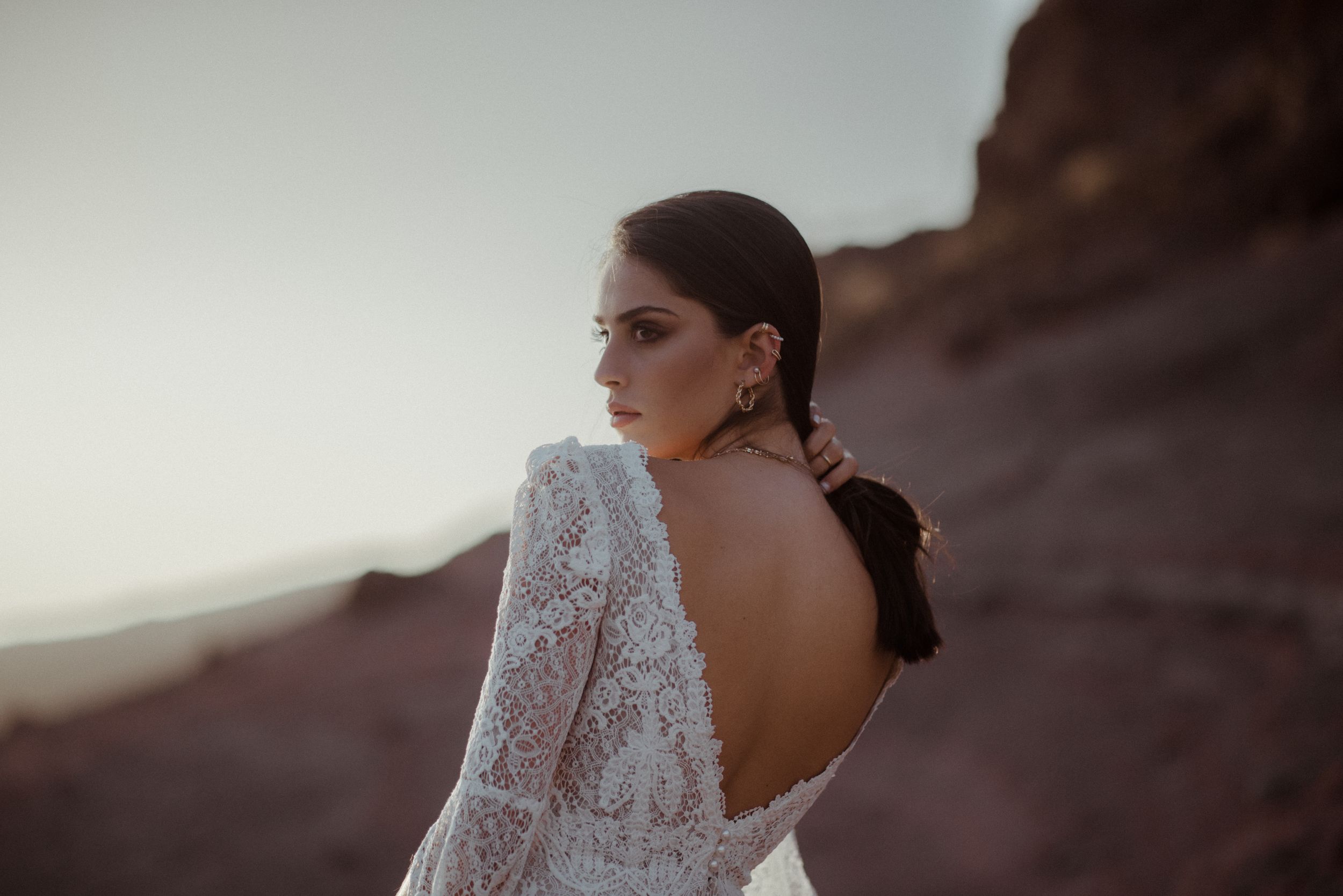 Open-back lace wedding dress photographed against mountain landscape at dusk.