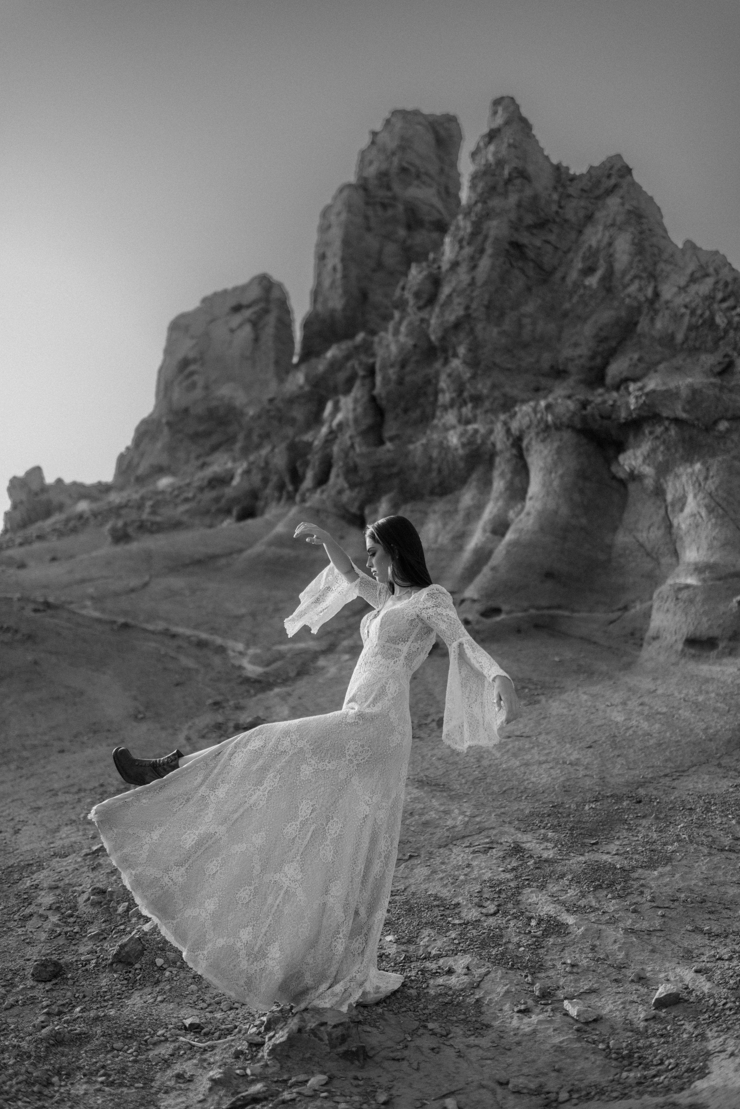 Ethereal white wedding dress flowing in the wind against dramatic rocky mountain backdrop in black and white.