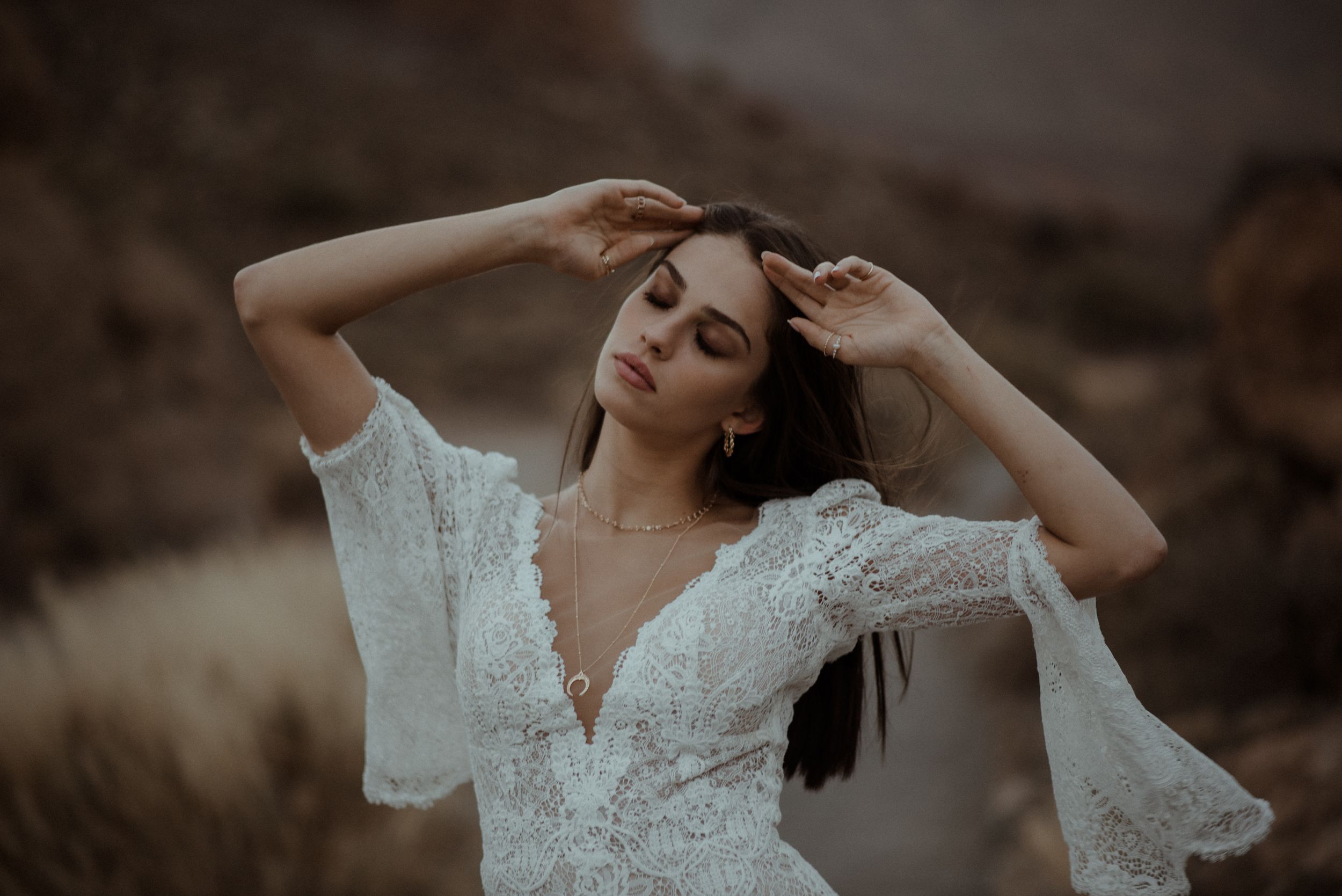 A delicate white lace wedding dress with bell sleeves is showcased against a moody desert landscape.