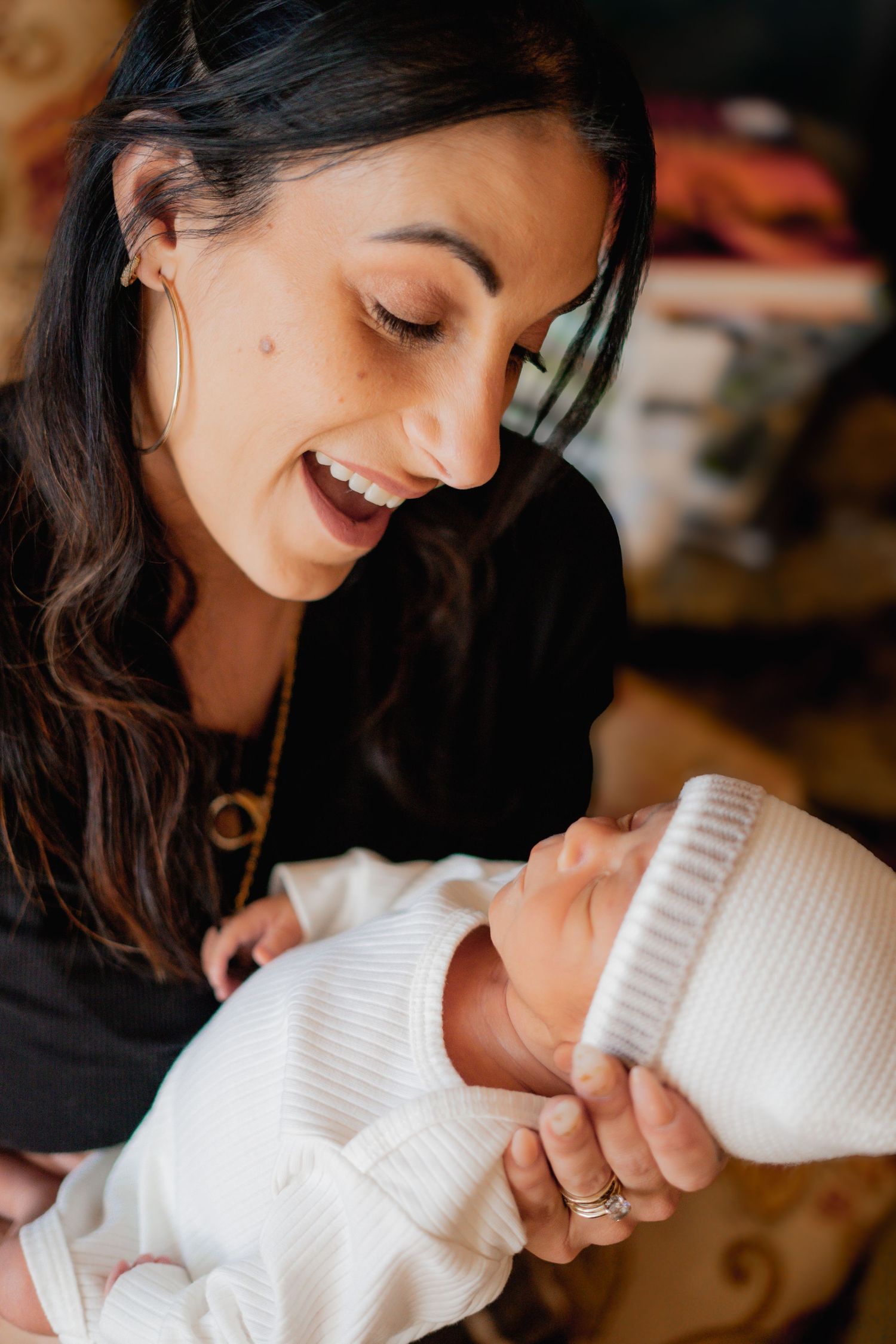 Parent shares tender moment while cradling newborn baby wearing white knit clothing in warm indoor setting.