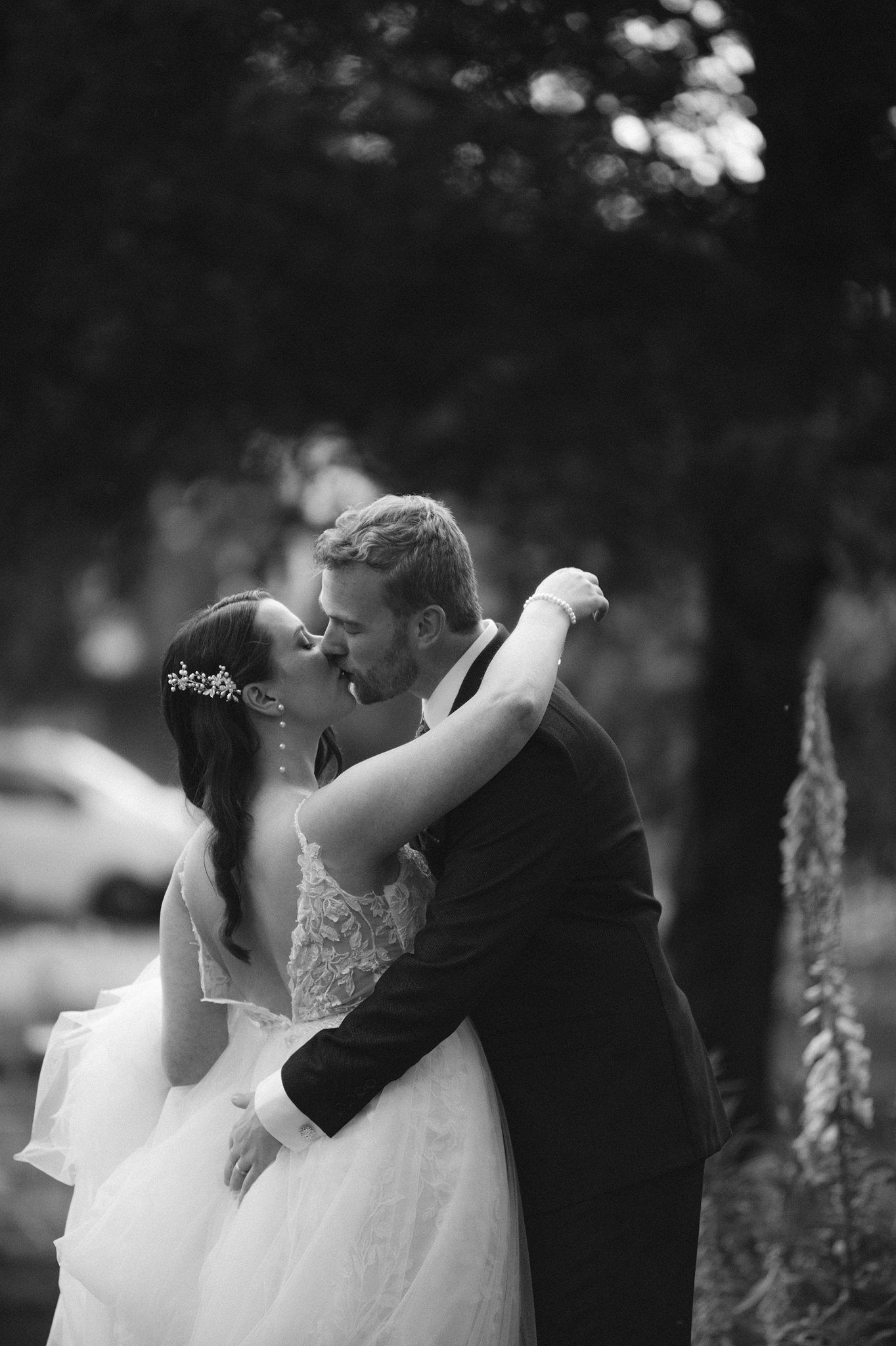 A romantic black and white wedding photo shows a couple embracing in a dreamy outdoor garden setting at the Tangled Garden, Grand Pre