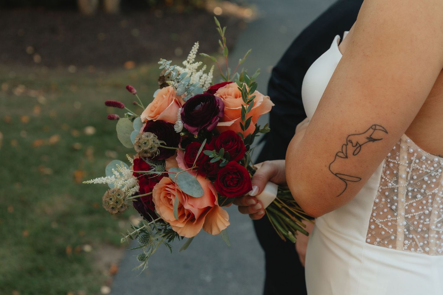Bride holding a stunning bouquet of burgundy, coral, and red roses with eucalyptus greenery on wedding day.