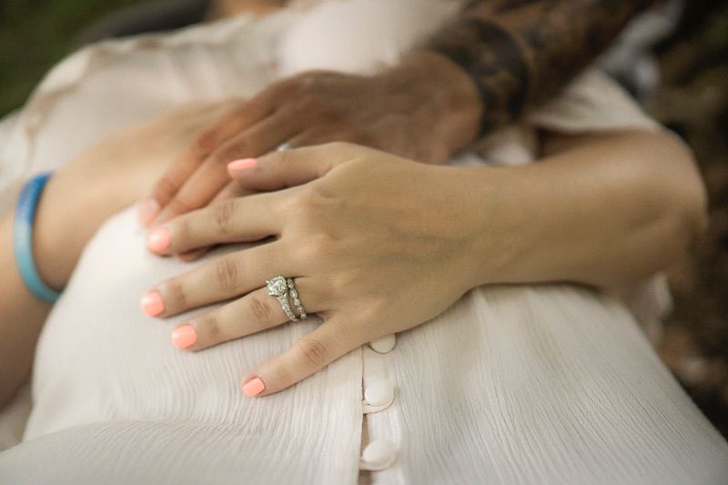 Close up of hands resting on white fabric showing an engagement ring and bracelet.