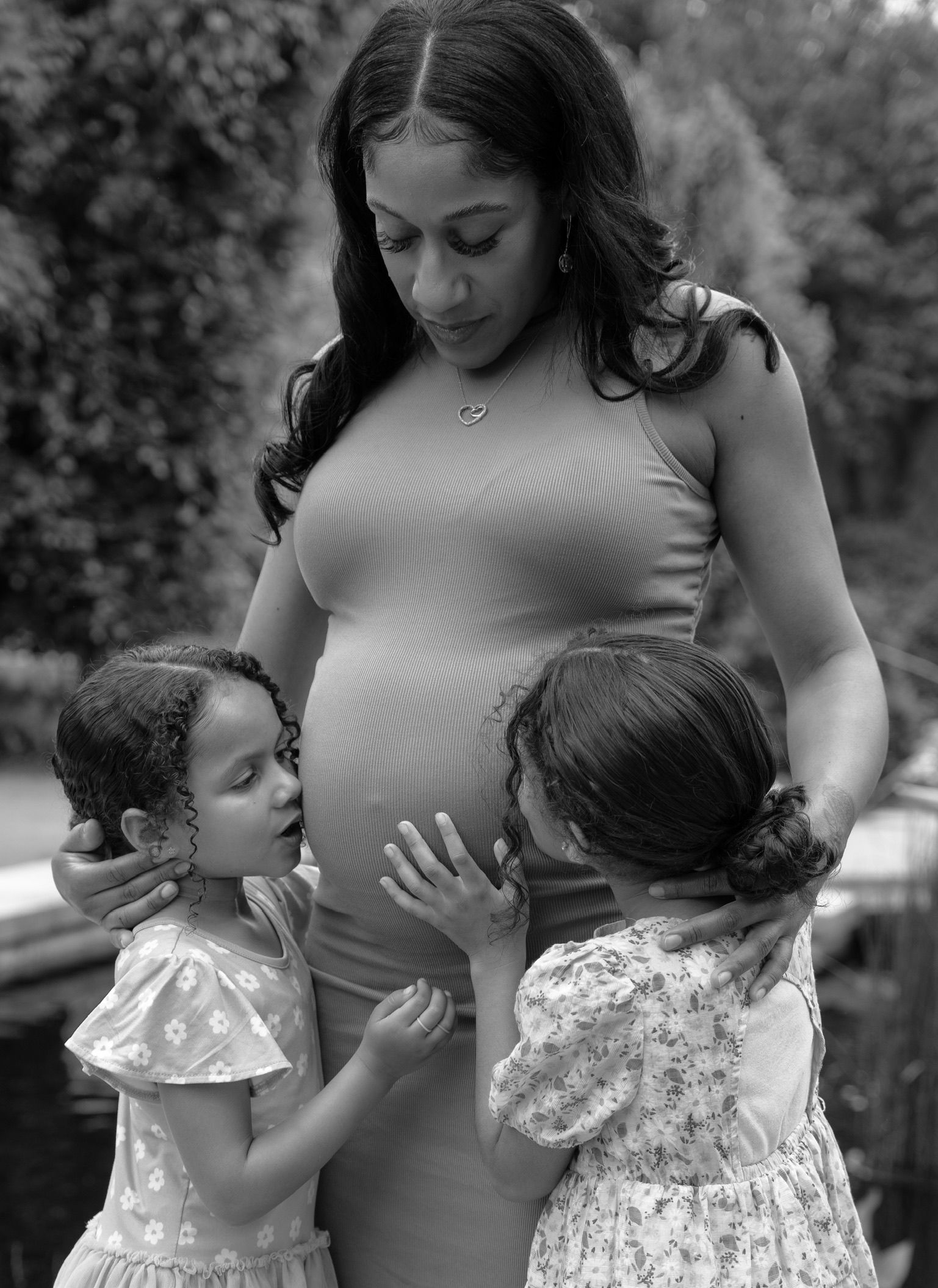 A tender moment as two young children interact with an expectant mother in a black and white portrait.