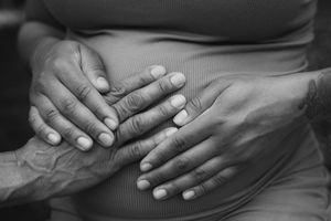 Close-up black and white image of hands tenderly cradling pregnant belly.