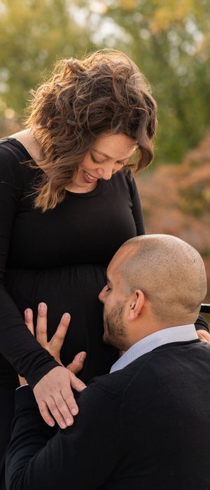 Couple sharing intimate moment during outdoor maternity photoshoot in autumn setting.
