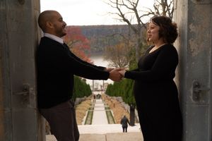 Couple sharing a romantic moment in an archway overlooking a garden path with fall foliage in the background.