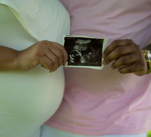 Hands holding ultrasound photo against soft pastel background.