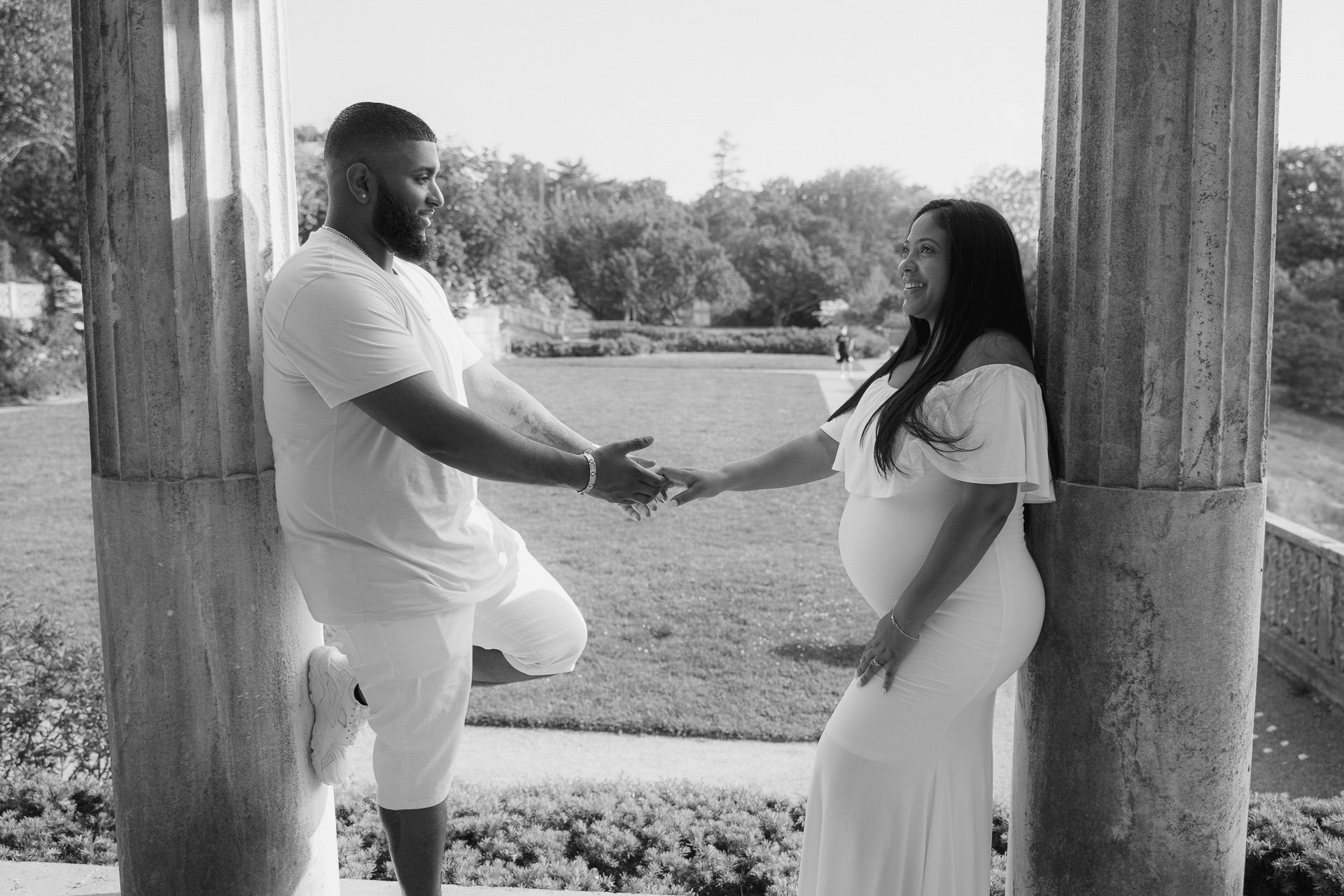 A couple in matching white outfits holding hands in an outdoor garden setting.